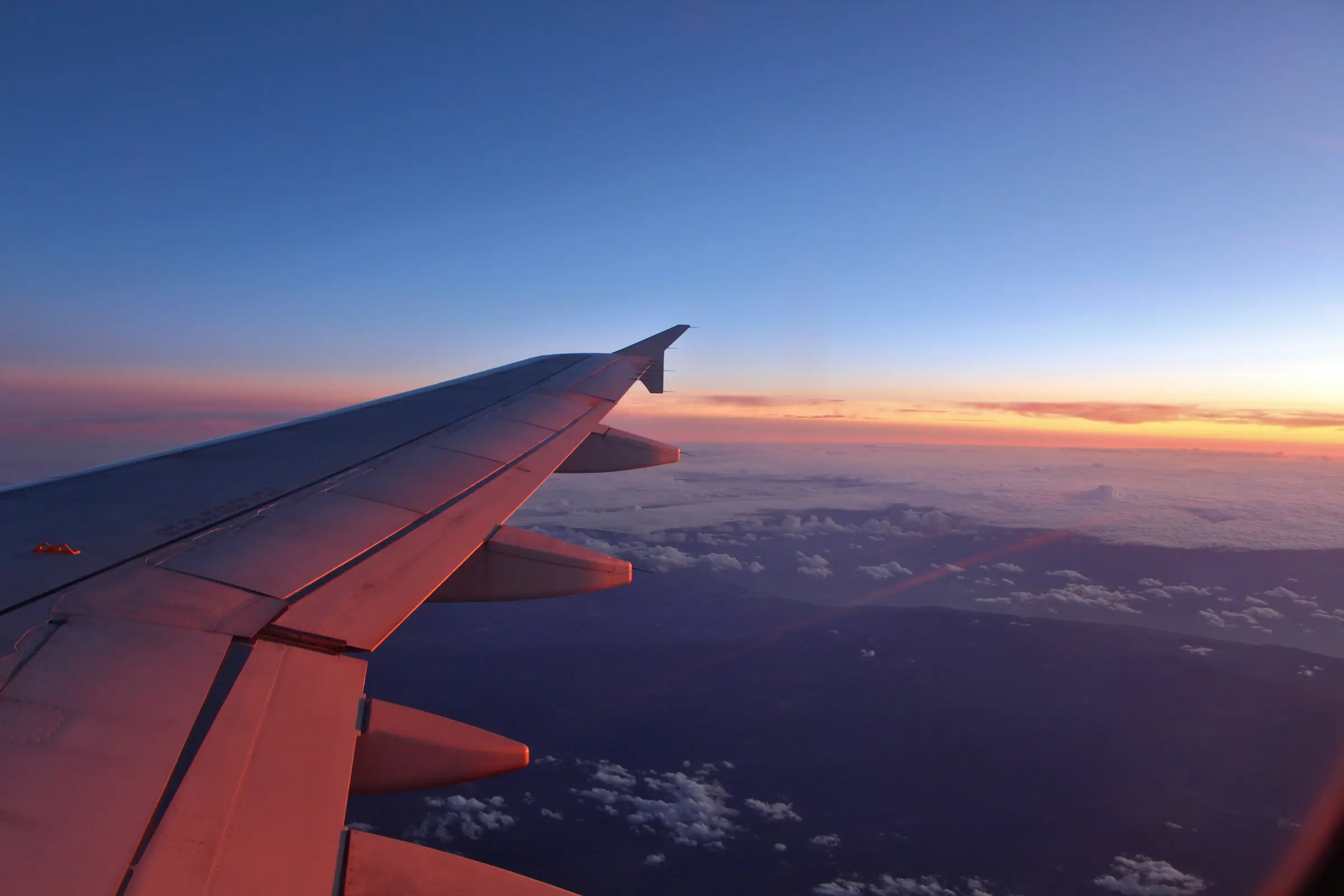 Blick aus dem Flugzeugfenster auf die Tragfläche bei Sonnenuntergang über den Wolken
